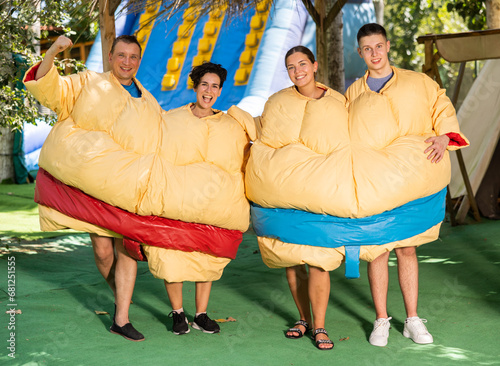 Young and adult men and women in large sumo suits having fun in adventure park, looking at camera and smiling. photo