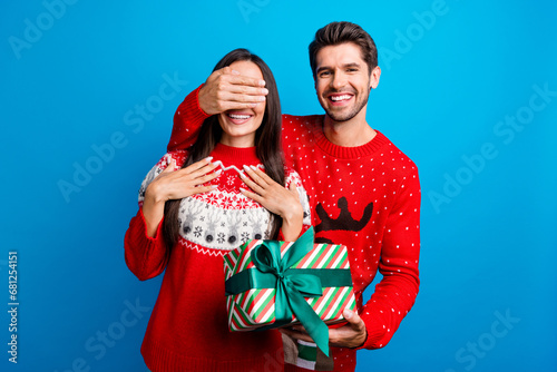 Photo portrait of lovely young spouses hold gift cover eyes surprise wear x-mas ornament red sweaters isolated on blue color background
