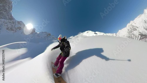 SELFIE, LENS FLARE: Happy woman enjoys snowboarding untouched snowy terrain on an adventure heliboarding trip in beautiful Albanian Alps. She has fun riding and spraying clouds of fresh powder snow. photo