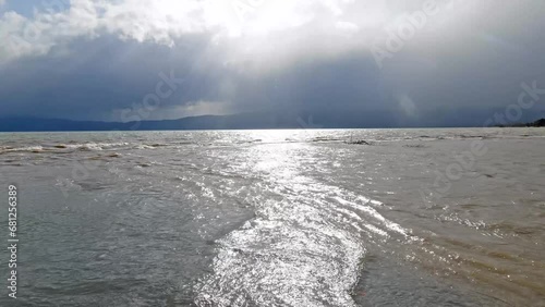 The sun breaks through the clouds and reflects off the waves of the lake