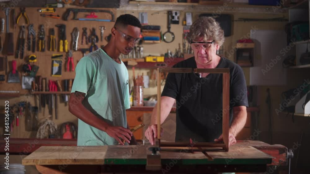 Carpenter working at workshop with the help of apprentice, small business worker doing woodwork in carpentry workplace Carpenter working at workshop with the help of apprentice, small business worker doing woodwork in carpentry workplace
