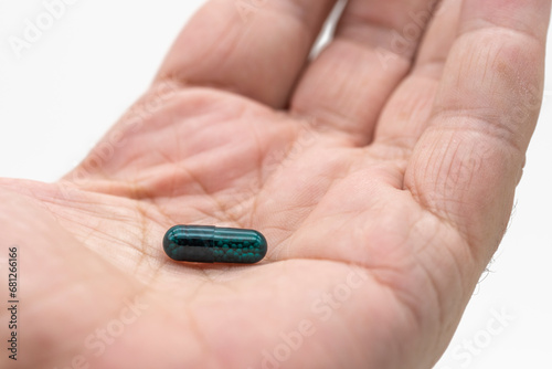Detalle de una píldora verde en la palma de la mano, aislado con fondo blanco