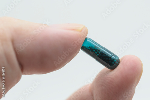 Detalle de una píldora verde entre los dedos de la mano, aislado con fondo blanco