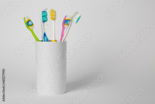 Different toothbrushes in holder on light grey background. Space for text