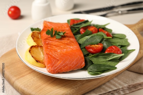 Tasty grilled salmon with basil, tomatoes and lemon on table, closeup