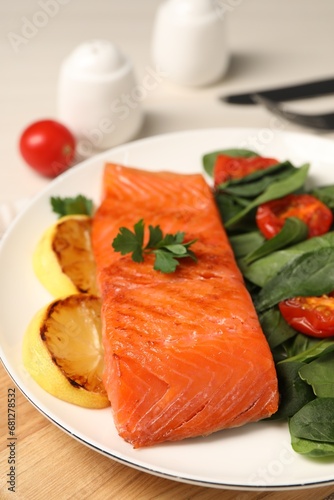 Tasty grilled salmon with basil, tomatoes and lemon on table, closeup