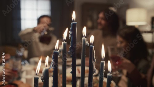 Close-up selective focus shot of nine burning candles on menorah on final day of Hanukkah holliday, and Jewish family of six having dinner together, smiling and talking in blurred background photo