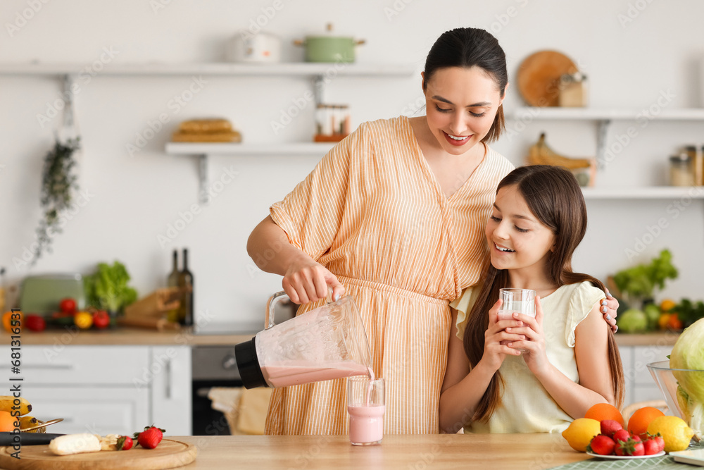 Young woman with her little daughter pouring fresh smoothie into glass in kitchen
