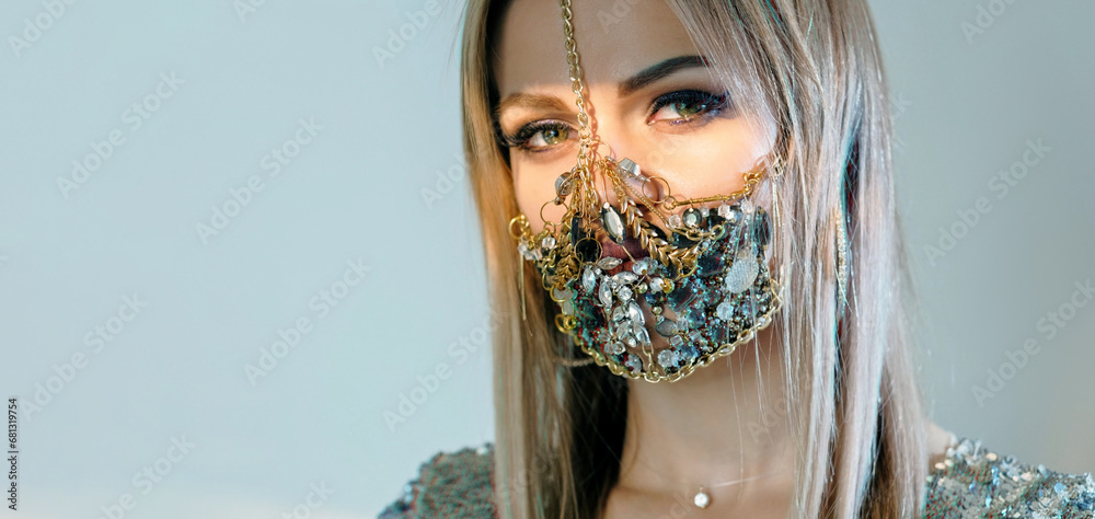 © golubovy - Pandemic fashion. Quarantine DIY accessories. Portrait of sensual woman in glamour handmade chain gemstone face mask posing isolated on blue copy space background.