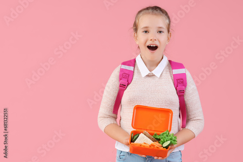 Shocked little girl with backpack and lunchbox on pink background