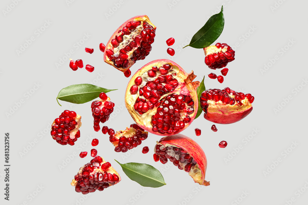 Flying fresh pomegranates with seeds and leaves on grey background Flying fresh pomegranates with seeds and leaves on grey background