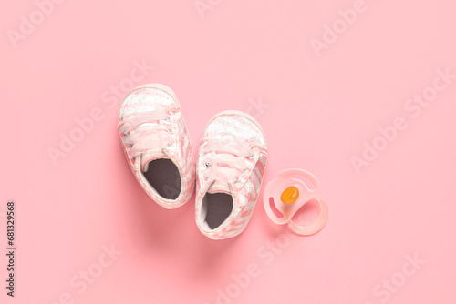 Stylish baby shoes with pacifier on pink background