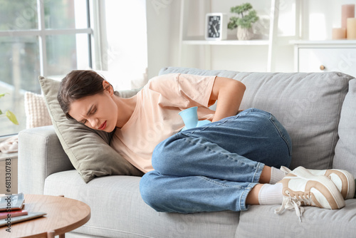 Photography Young woman with hot water bottle lying on sofa and suffering from abdominal pai