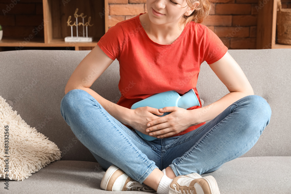 Fototapeta premium Young woman with hot water bottle suffering from stomach ache at home