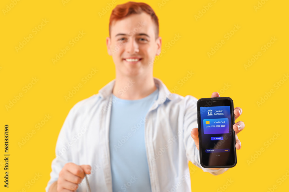Young man with mobile banking and shopping bag on yellow background Young man with mobile banking and shopping bag on yellow background