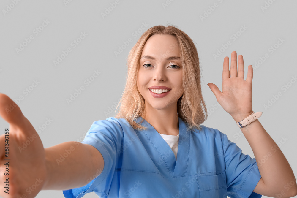 Fototapeta premium Beautiful female doctor waving hand and reaching out for handshake on grey background