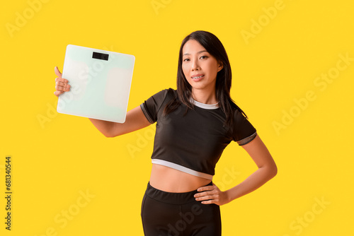 Beautiful young Asian woman with scales on yellow background. Weight loss concept