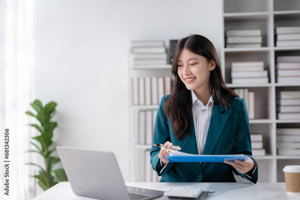 Financier working with documents at workplace. Young Asian business woman sitting working in modern office with documents and laptop computer. Financier working with documents at workplace. Young Asian business woman sitting working in modern office with documents and laptop computer.