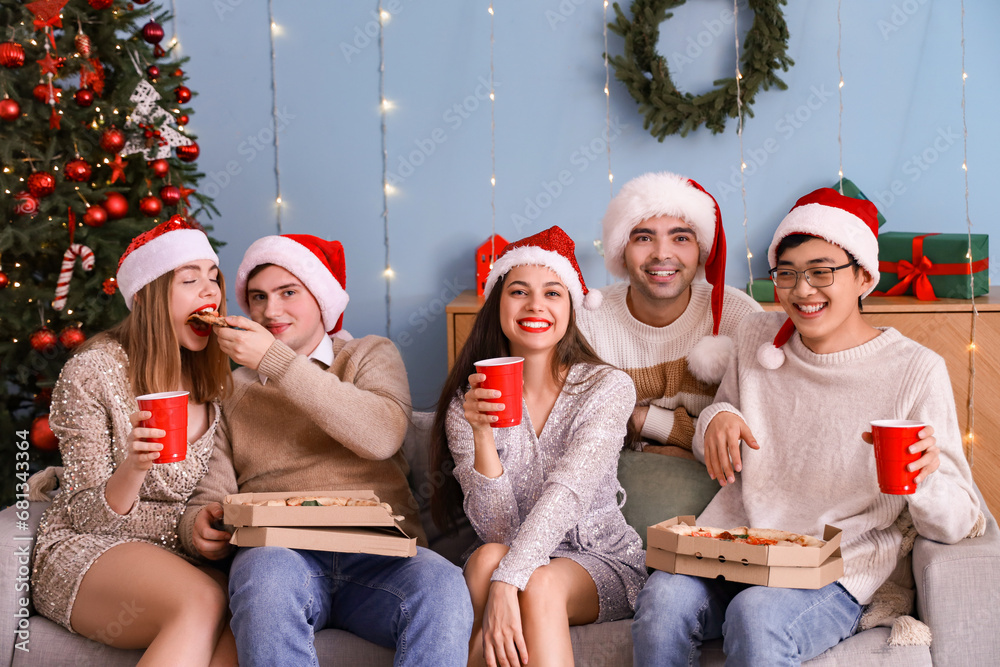 Obraz premium Group of young friends with pizza celebrating Christmas at home party