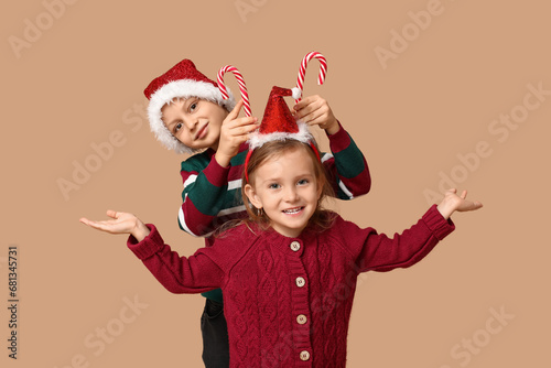 Funny little children in Santa hats with candy canes on beige background