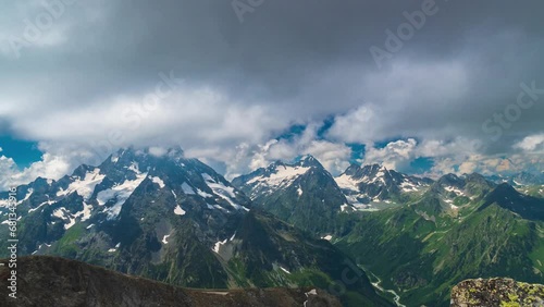 Dark rain clouds gather over the mountains. The mountainsides are green and the peaks are covered with snow and glaciers. Summer weather changes in the mountains. Smooth recoil with the camera photo