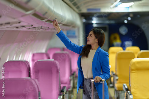 Businesswoman, confident tourist walks with suitcase, checks seat, flight number, puts her suitcase on shelf inside airplane travel lifestyle concept.