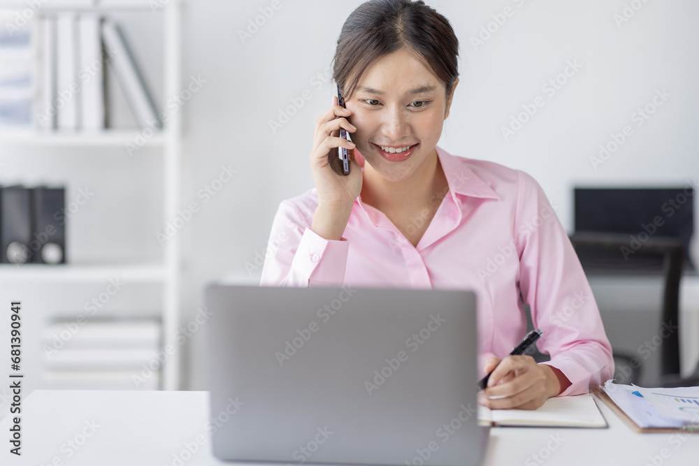 Young asian woman talking on the phone while working on computer in desk office. Searching on internet Young asian woman talking on the phone while working on computer in desk office. Searching on internet