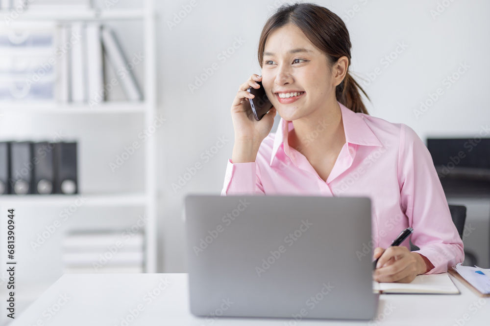 Young asian woman talking on the phone while working on computer in desk office. Searching on internet Young asian woman talking on the phone while working on computer in desk office. Searching on internet