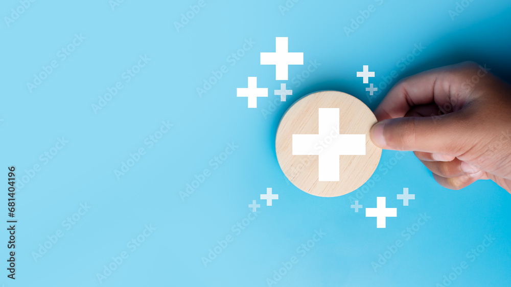 Obraz premium Human hand holding a piece of wood with a plus sign representing positive things such as profits, benefits, development, CSR represented by a plus sign, health insurance. Hand showing a plus sign.