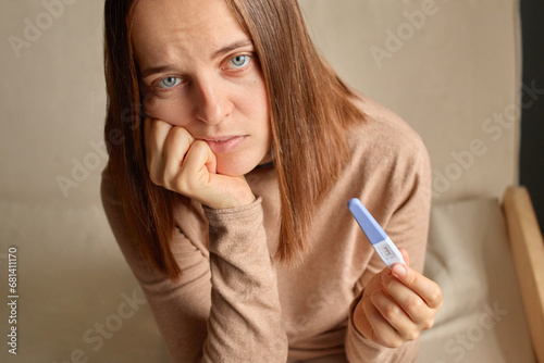 Sad upset unhappy woman hand holding pregnancy test with two stripes positive result future mother waiting for childbirth.