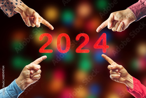 2024, People pointing to the number 2024 on background of faded lights. Happy New Year