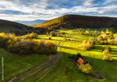 Fototapeta Naklejka Na Ścianę i Meble -  Aerial view in summer in Slovakia. Ggreen meadows and fields, grass and trees, rural road at dawn in spring. Top drone view of mountain countryside