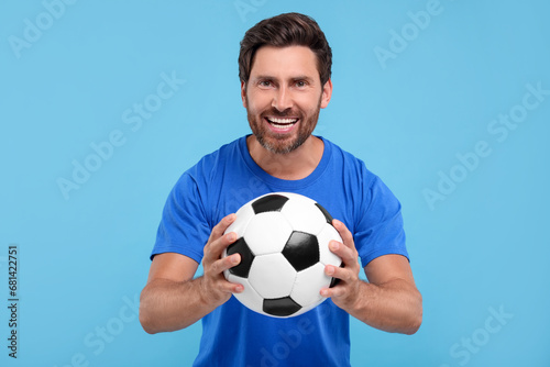 Emotional sports fan with soccer ball on light blue background © New Africa