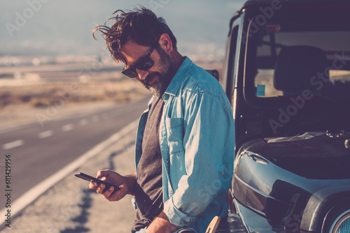 Traveler man use phone mobile cnnection standing against a black off road car with long road in background. Road trip and travel lifestyle for adventurer male people. Use of digital map road trip
