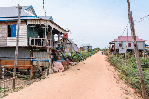 Houses made from corrugated iron on wooden stilts in a poor, rural village with a dirt track road in Cambodia.