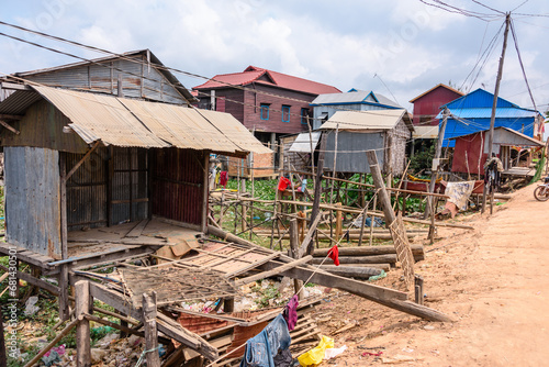 Houses made from corrugated iron on wooden stilts in a poor, rural village with a dirt track road in Cambodia.