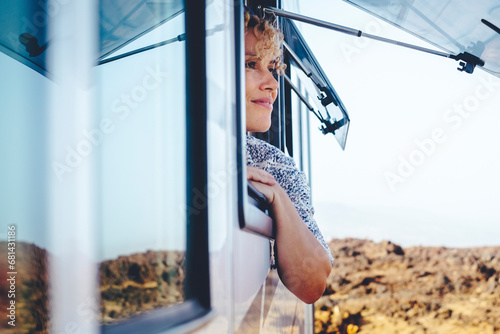 Nice adult woman smile and enjoy freedom at the natural campsite admiring outdoors outside the window of her camper car. Concept of summer tourist travel vacation and free female independence people photo