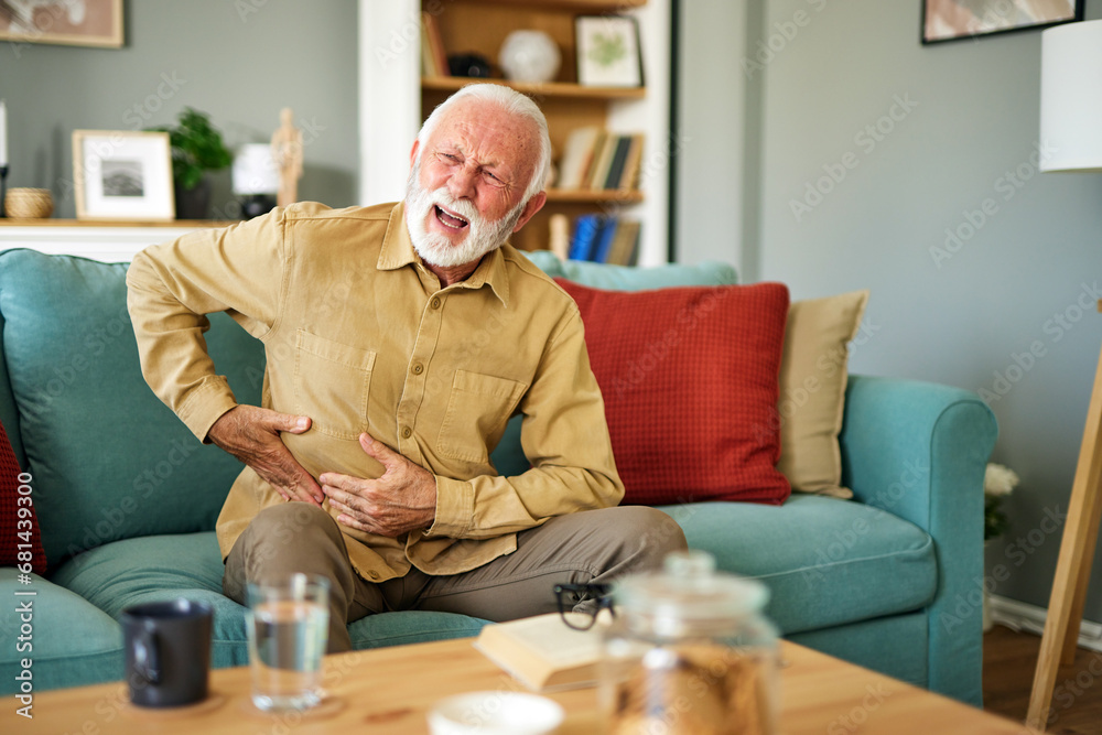 Senior man suffering from stomach ache sitting on a couch in the living room at home