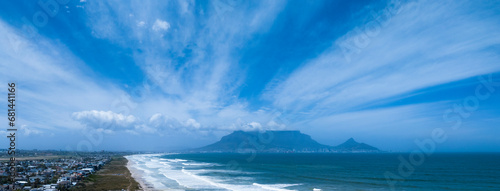 Aerial wide view of Table Mountain in Cape Town on a sunny day, clouds billowing over the mountain and beach in foregound. photo