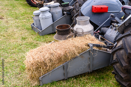 Milk churns and a bale of straw on the rear of a vintage tractor.