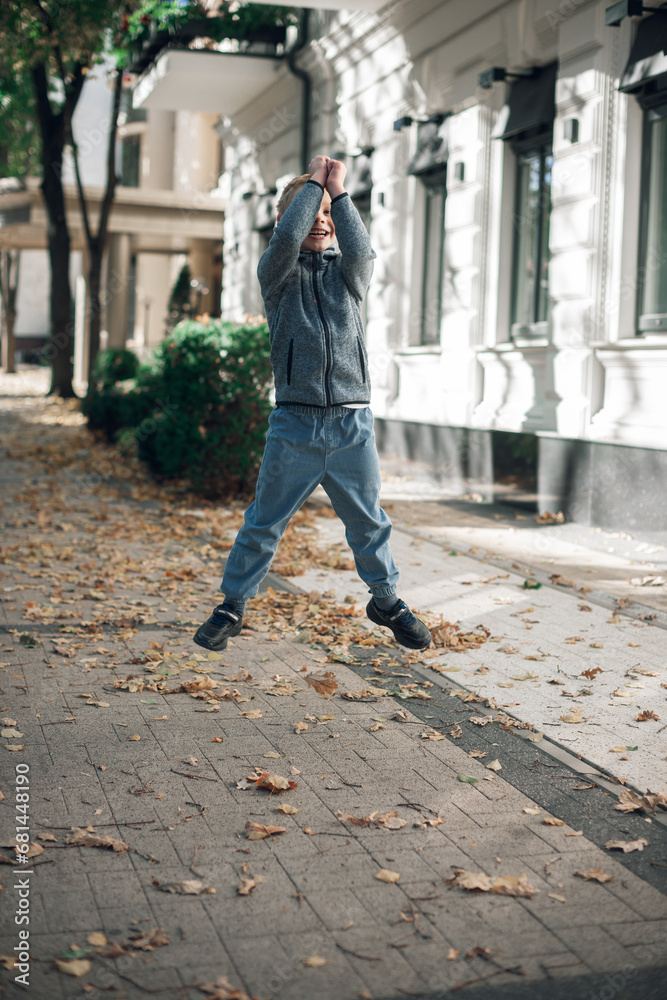 photo of a boy in a high jump on the streets of an autumn city. wearing a blue jacket and blue jeans