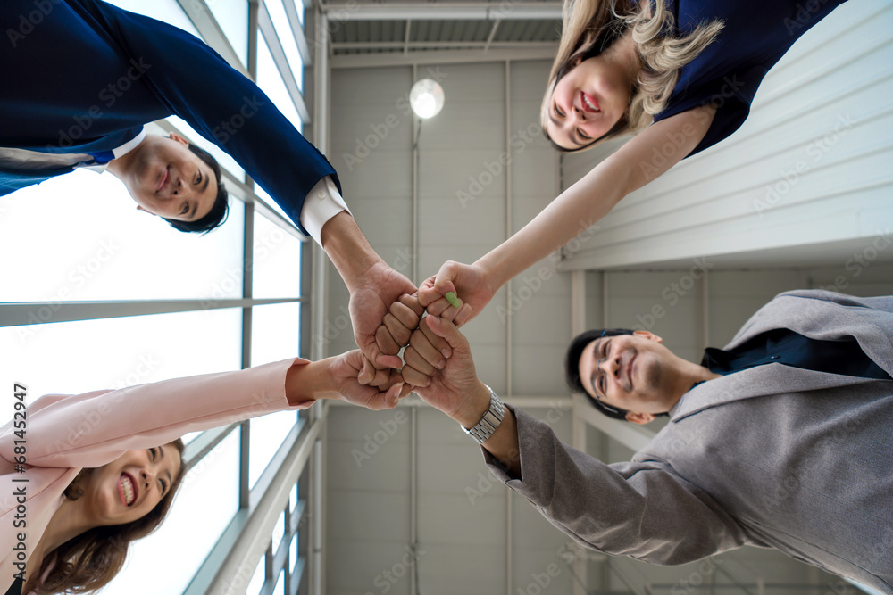 Team building concept. Coworker standing in circle bumping fist together, celebrating business success in modern office with high ceiling. Bottom View - obrazy, fototapety, plakaty 
