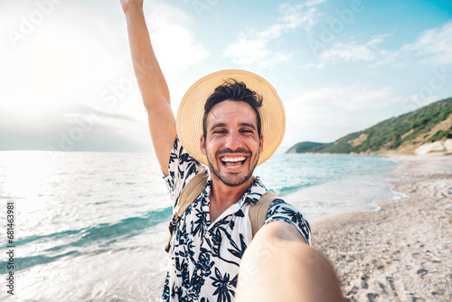 Handsome young man taking selfie picture with smart mobile phone outside - Happy tourist enjoying summer holiday at the beach - Traveling and technology life style concept photo