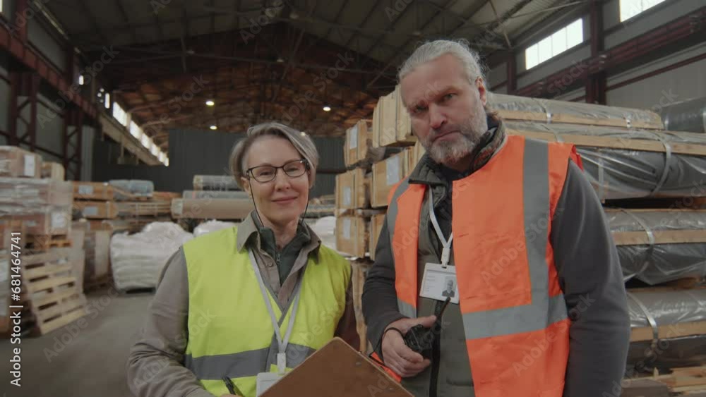 Portrait of couple of storage workers wearing reflection clothing discussing business paper and looking at camera Portrait of couple of storage workers wearing reflection clothing discussing business paper and looking at camera