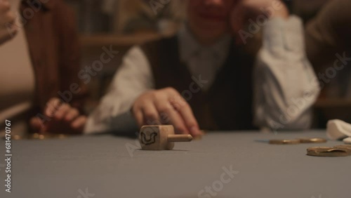 Close-up shot of hand of unrecognizable Jewish woman spinning wooden dreidel toy on table during Hanukkah festival, with visible Hebrew letters Shin - put in gelt coin, and Nun - nothing photo