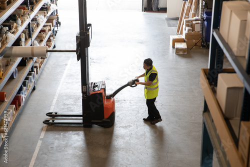 Worker in a warehouse using machinery to lift product photo