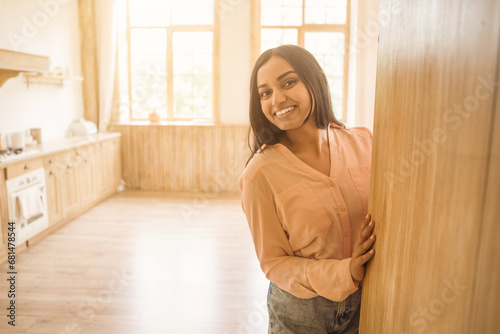 Smiling indian woman leaning on door frame in kitchen