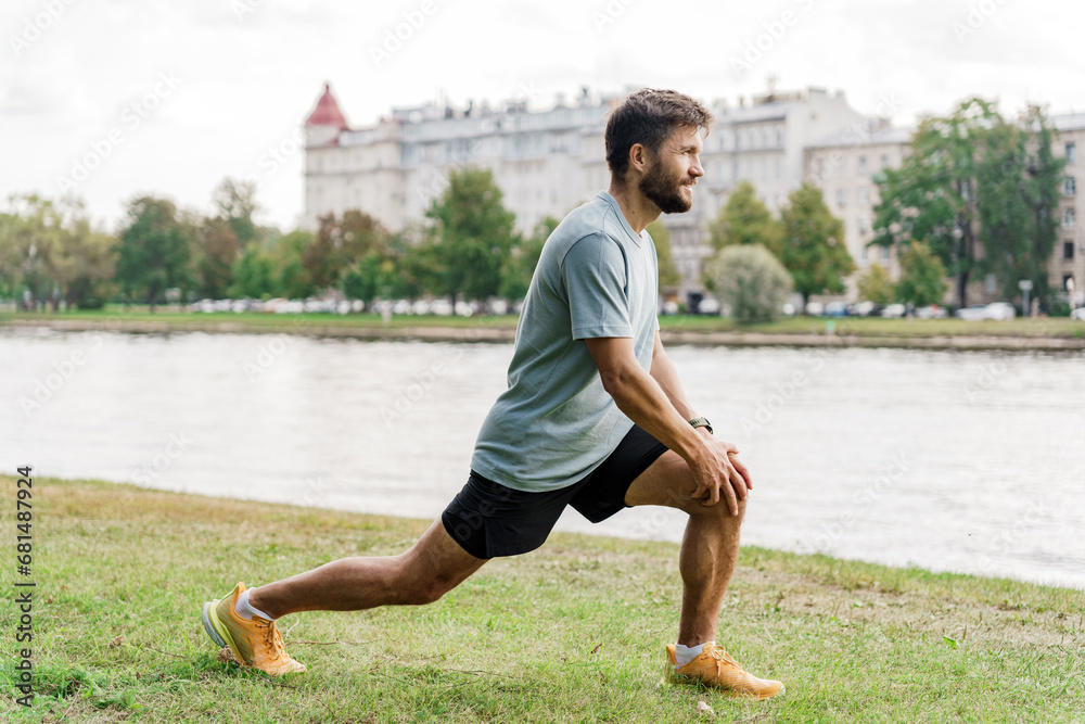 Fototapeta premium Body warm-up A running man is a sporty, slender young man in a T-shirt, shorts. Interval training for running alone in the park.