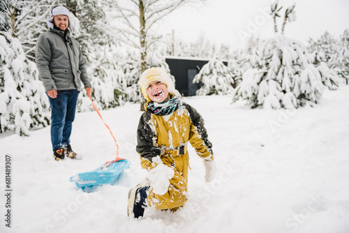 Kid fall into snow, lie. Dad pulling little son on winter day. Children are rolling down hill on sledge in forest. Happy child with father ride sled on snowy road. Family walks during snowfall in park