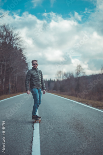 Cool hipster guy or man riding a longboard in the middle of the road in epic atmosphere. Freedom while riding a longboard, movie like setting. Long stretch of straight road, autumn setting.